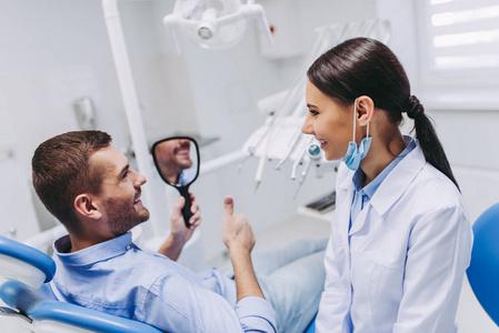 微笑的男性病人看着镜检查牙术后的临床应用照片