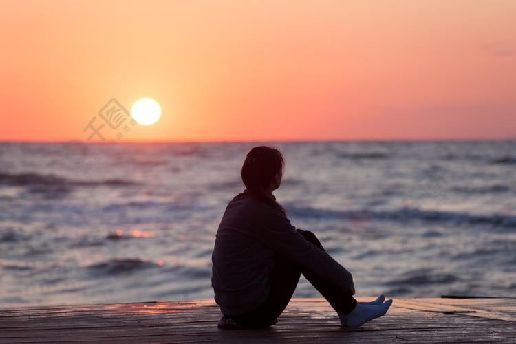 孤独的女孩坐在日出海滩上日出天空上的女人剪影