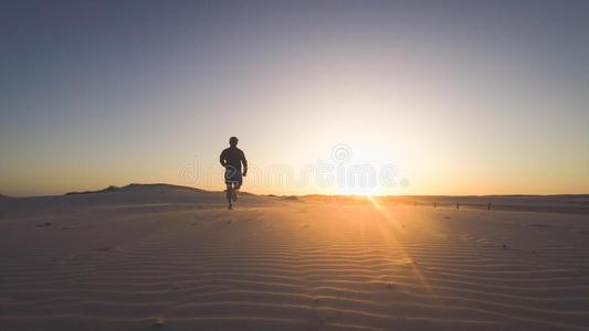 硬汉图片背影日落时分,跑步者在沙滩上奔跑的背影,背景是太阳.