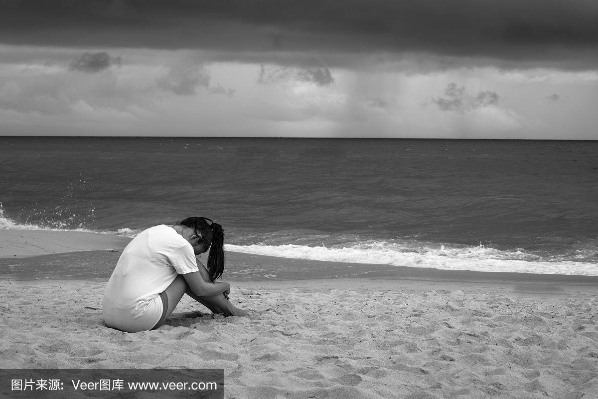 年轻悲伤的女人坐在海滩上在雨中哭泣.黑色和白色