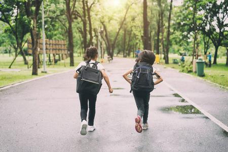 两个小学生跑去上学.两个背着书包的女孩.温暖的秋天的一天.回到学校.