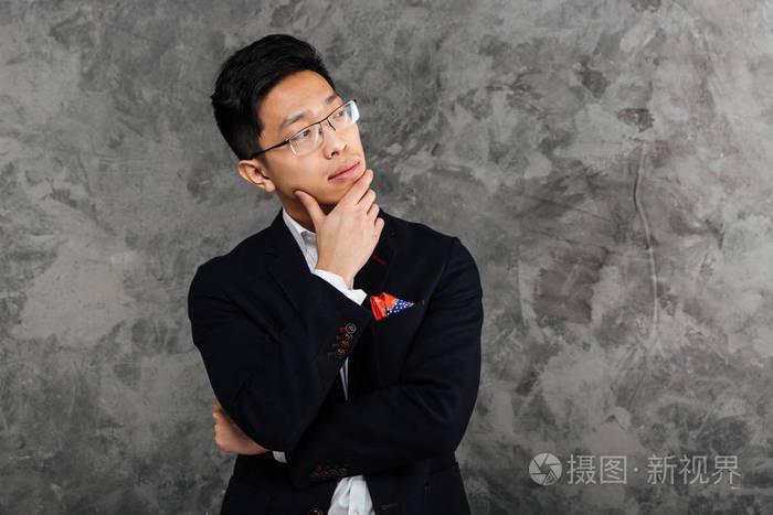一个沉思的年轻亚裔男子身着西装思考的肖像