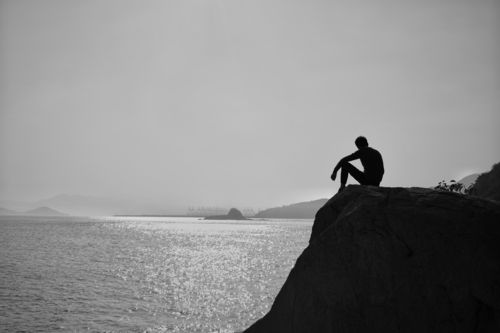 海岸线旁,一个男人坐在礁石上,仿佛在演绎着孤独.