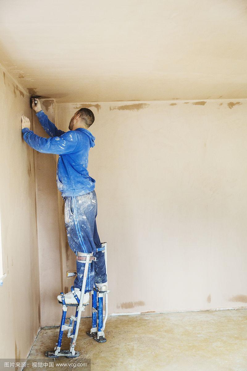一名抹灰工人戴着高脚柱,抹平正在施工的房屋墙上的新灰泥.