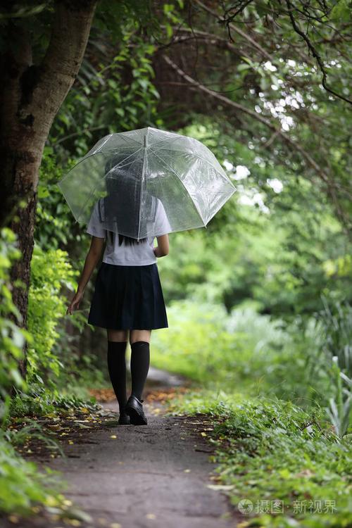 亚洲女孩的肖像,带着雨伞在雨中的自然人行道上散步