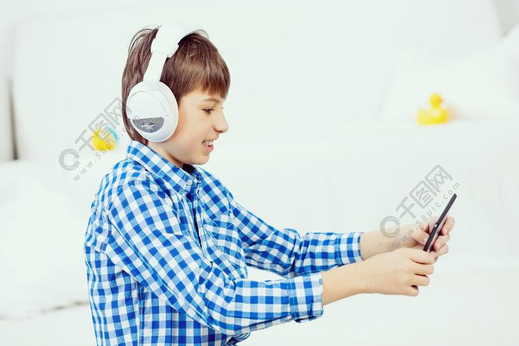 孩子享受闲暇时间入学年龄的男孩戴着耳机在玩平板电脑游戏的头上