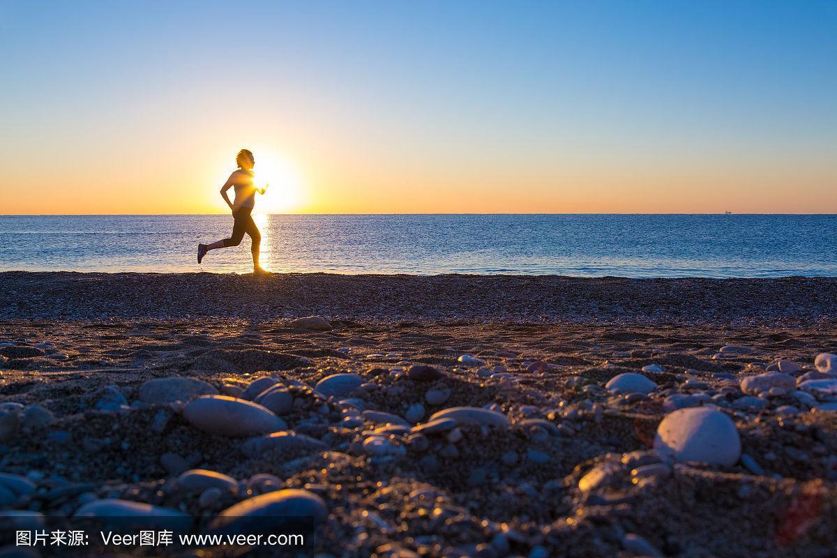 日出时沿海洋海滩慢跑的人类剪影
