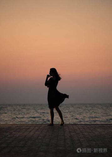 一个女孩在日落背景(日出)上的剪影在海平线上. 夏天在海滩上散步.