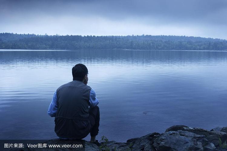 一个人坐在忧郁,孤独的蓝色湖边沉思