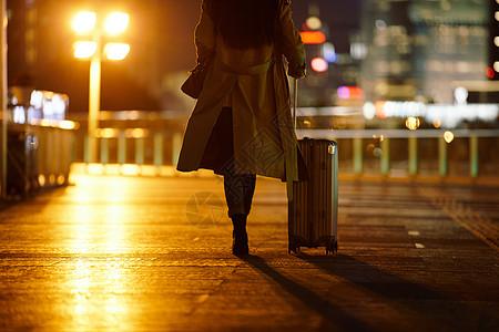 背影行李箱夜晚都市女性手提行李箱走在路上背景