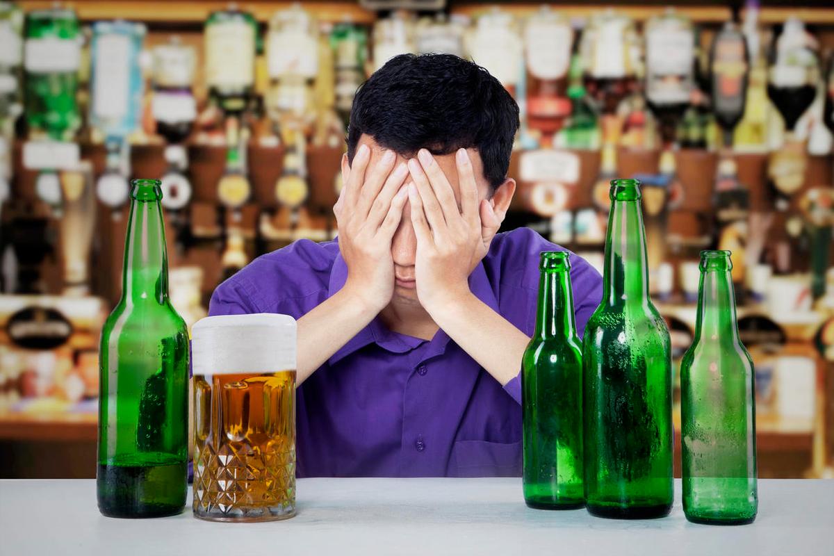 悲伤酗酒的男人用啤酒樽及玻璃在一家酒吧的桌子上后悔