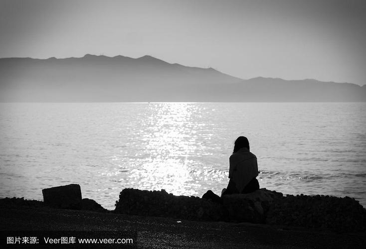 抑郁症.一张忧郁的女孩独自坐在海边,悲伤而沉思的黑白照片