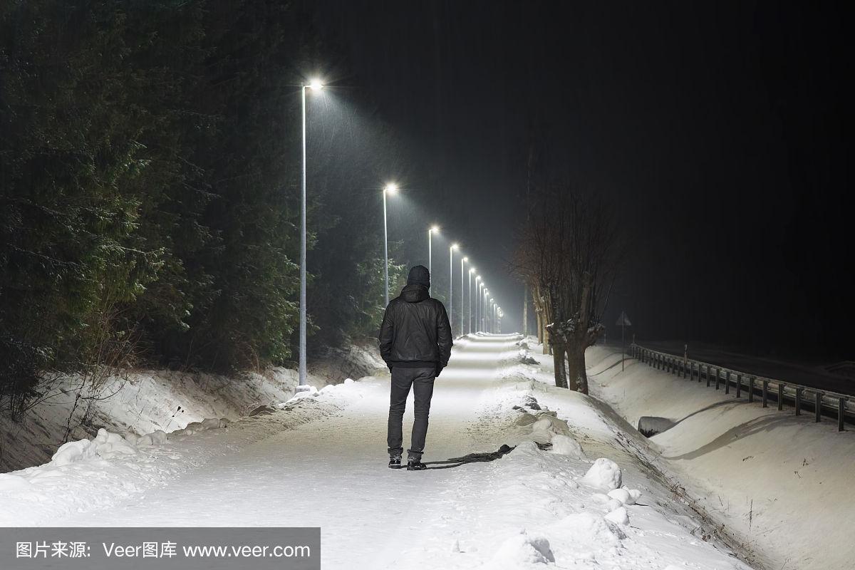 在白色的路灯下,一个年轻人独自慢慢地走在白雪覆盖的人行道上.
