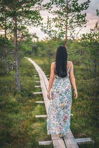 孤独的年轻女子穿着衣服独自行走在森林中的木制小路上日落