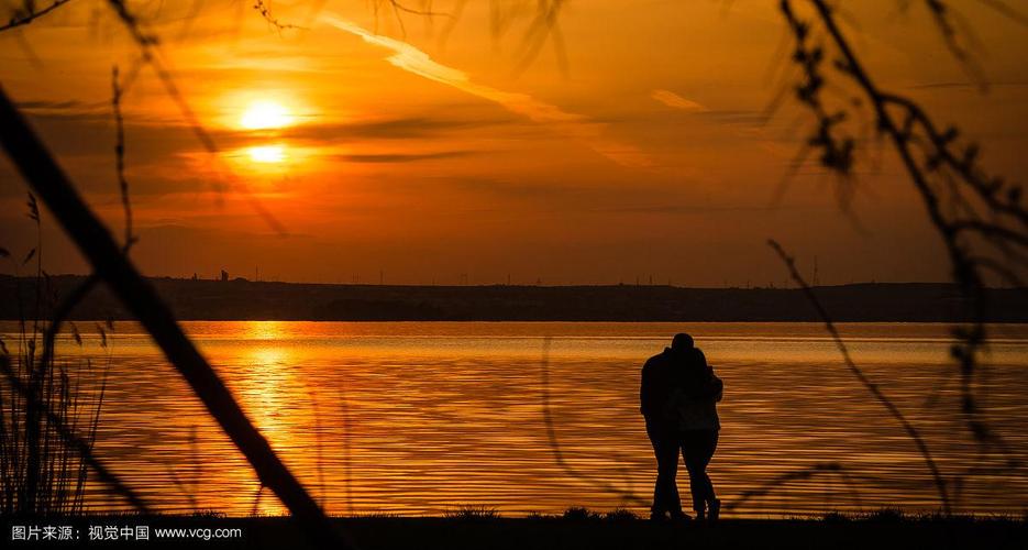 忧郁的日落时分,一对情侣在湖边拥抱的剪影