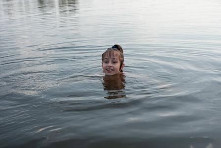 快乐美丽的小女孩在蓝色的水里游泳,露出水面微笑.
