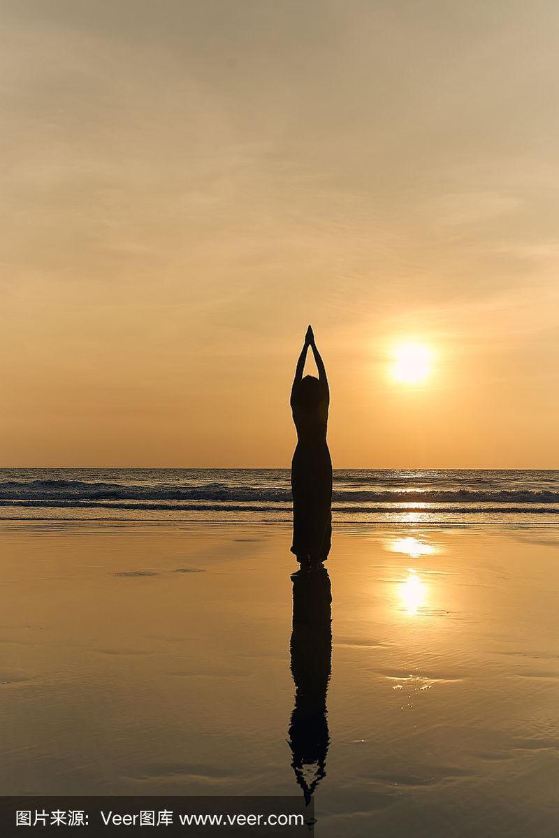 一个女人穿着漂亮的长裙,在日落的海滩上做瑜伽.