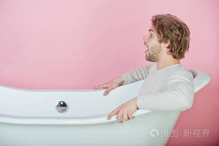 英俊的惊讶的年轻人穿着内衣坐在白色的浴缸