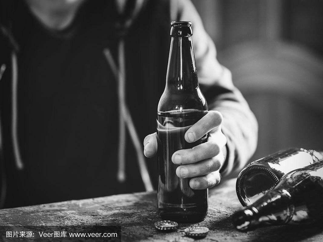 一个男人拿着一瓶啤酒独自喝酒的特写