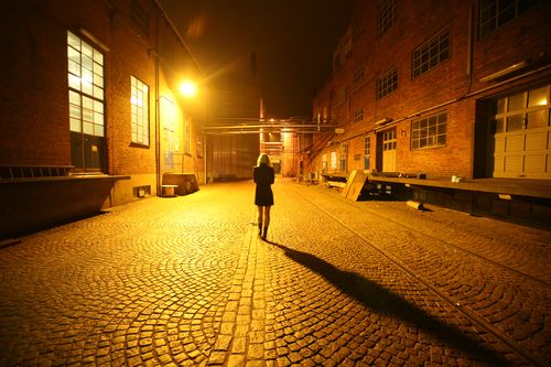后面看法照片的女人独自走在鹅卵石巷子里面在晚上