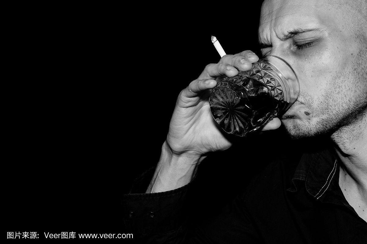 醉汉一边喝酒一边抽烟.黑色和白色.黑暗的形象.黑色背景.