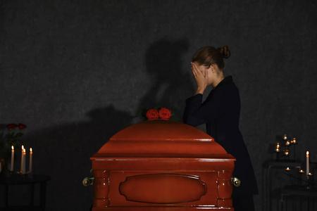 一位悲伤的年轻女子在小教堂里用红玫瑰在灵柩旁哀悼照片