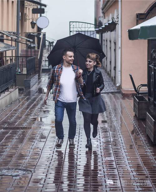 一对相爱的年轻夫妇在雨天一起撑伞跑步