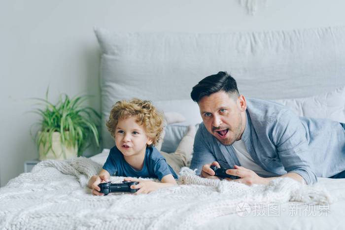 爸爸和孩子在家里的床上玩游戏按下游戏杆上的按钮