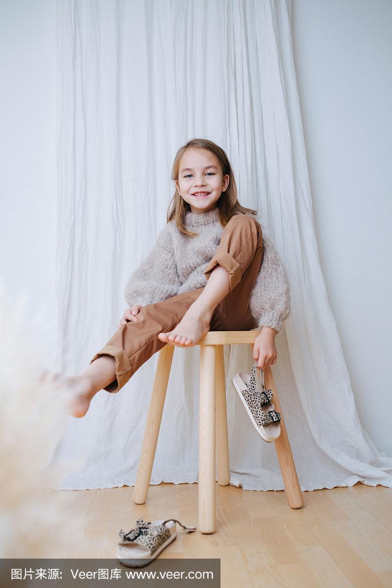 快乐的小女孩坐在凳子上,脱下赤脚上的凉鞋