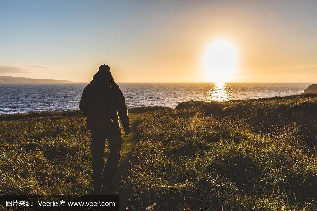 一个背着背包的男人在夕阳下走向大海